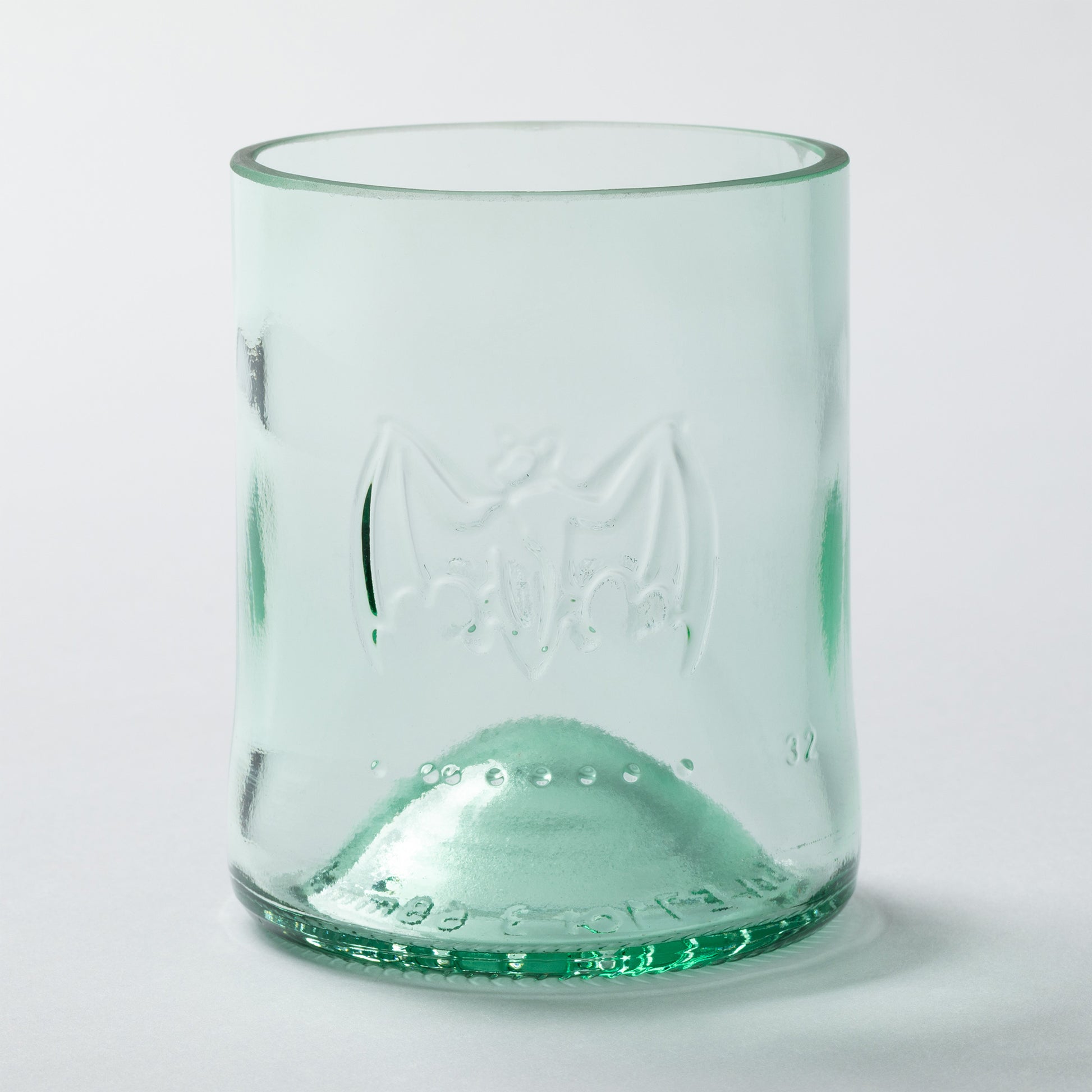 Green glass tumbler made from recycled glass with embossed design on a white background