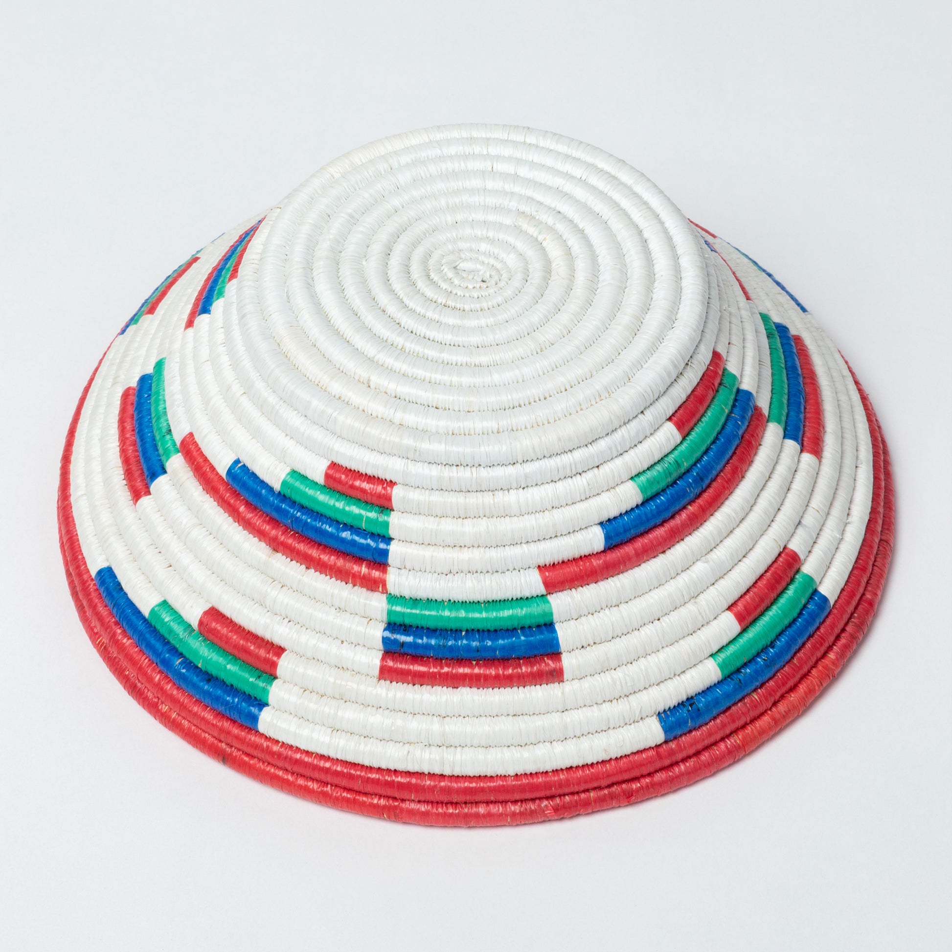 Colorful woven basket turned upside down with white, red, blue, and green patterns on a light gray background