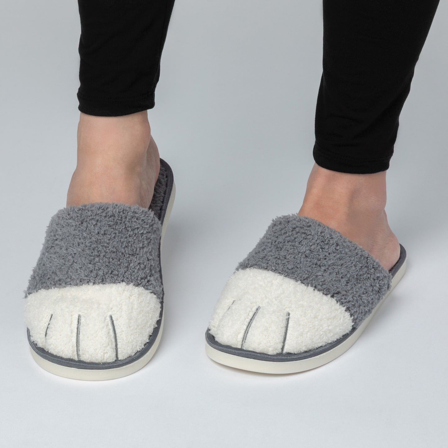 Gray fuzzy slippers with white soles worn by a person on a light gray background