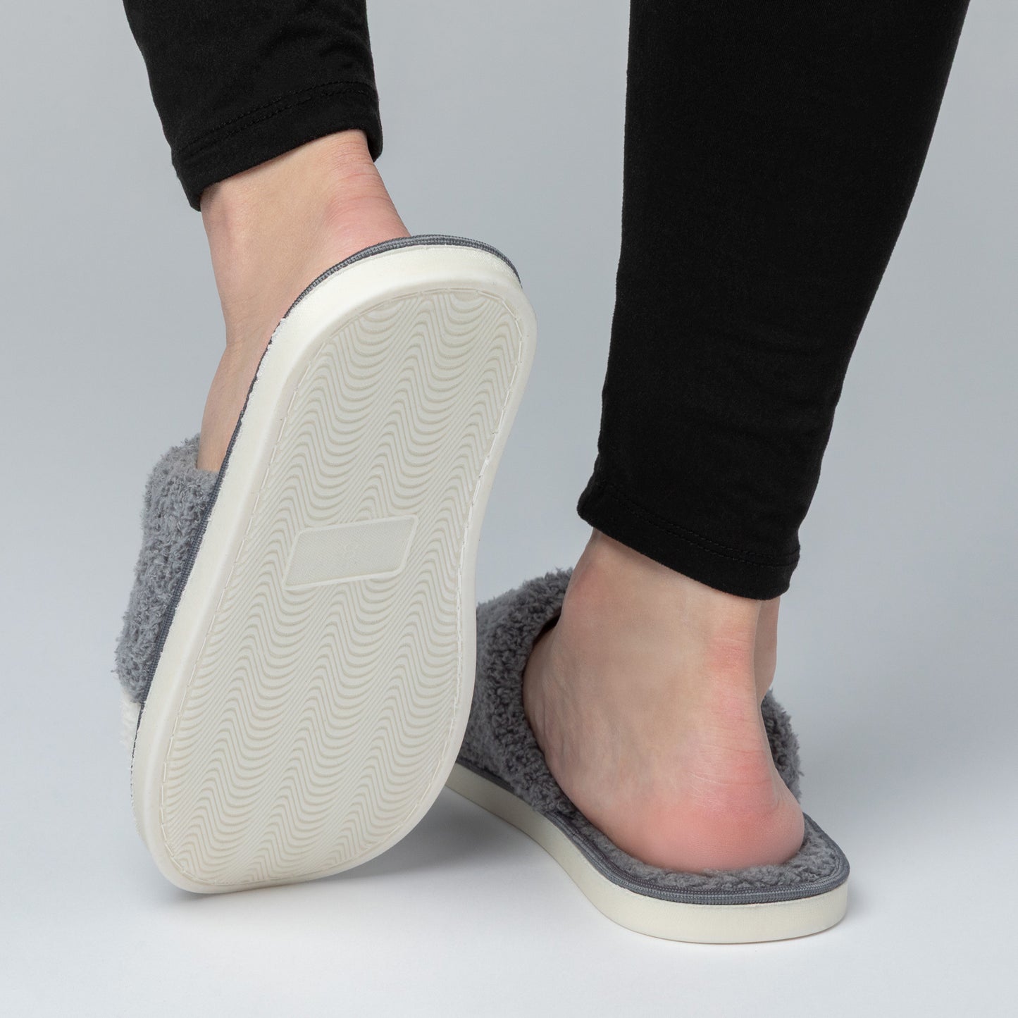 Gray slippers worn with black pants on a gray background