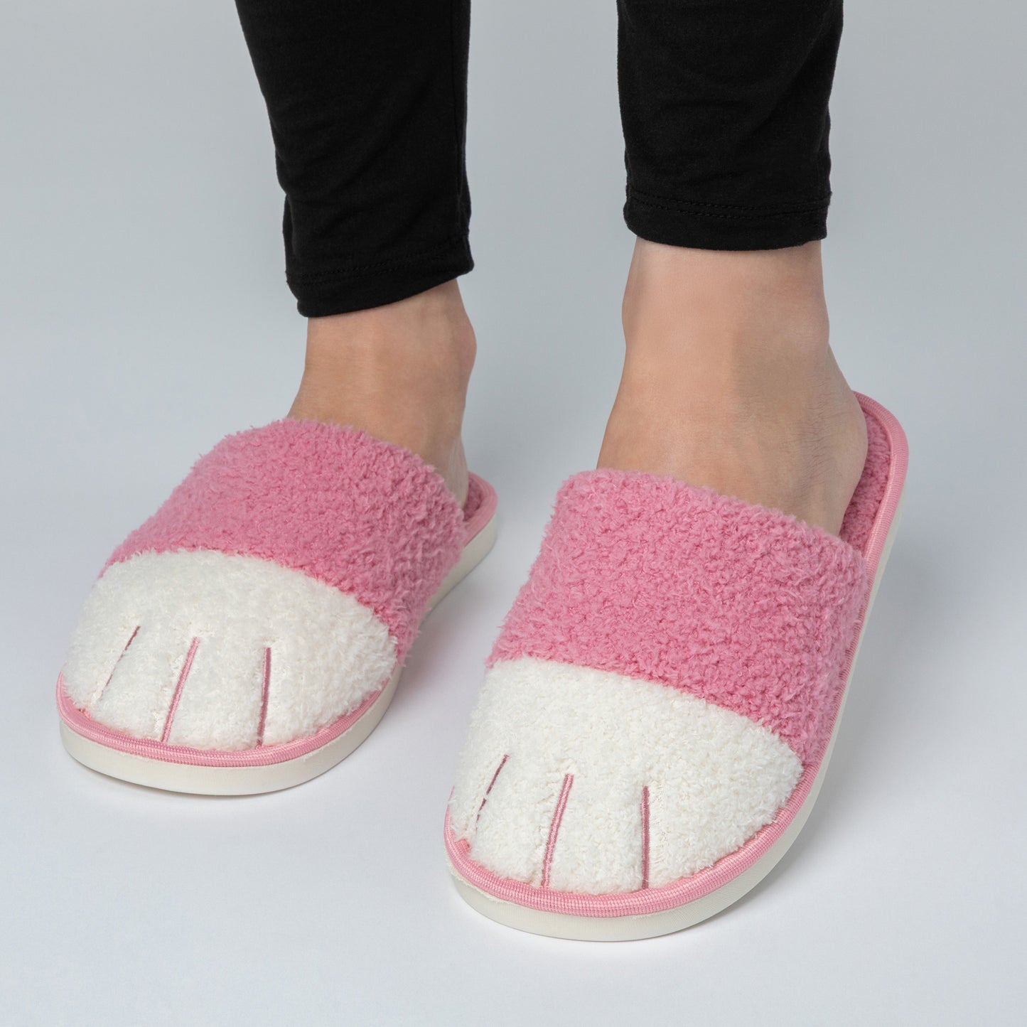 Pink and white slippers worn with black pants on a light gray background