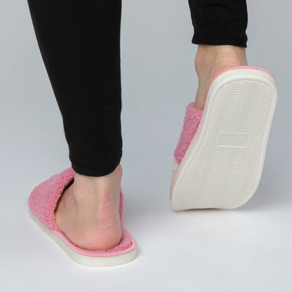 Pink slippers with white soles worn by a person on a gray background