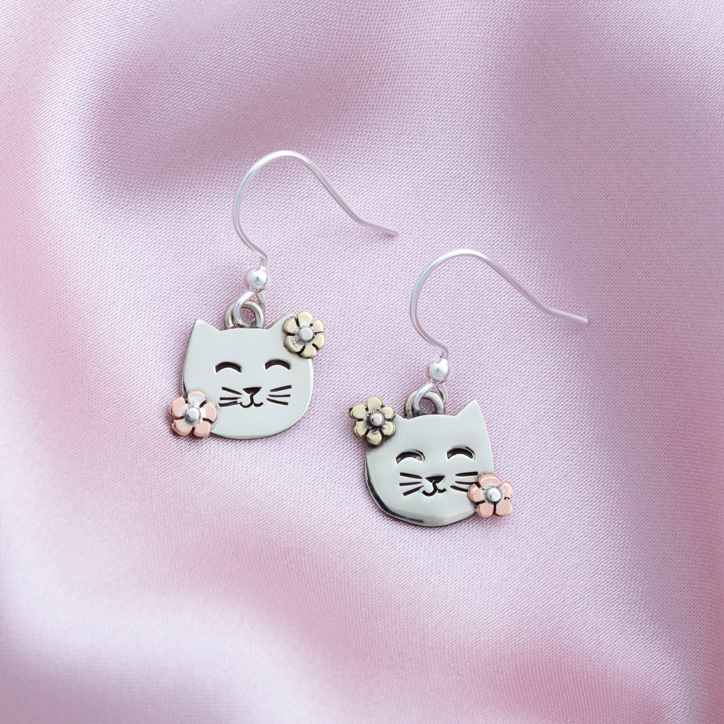 Cat-shaped earrings with floral details on a pink satin background