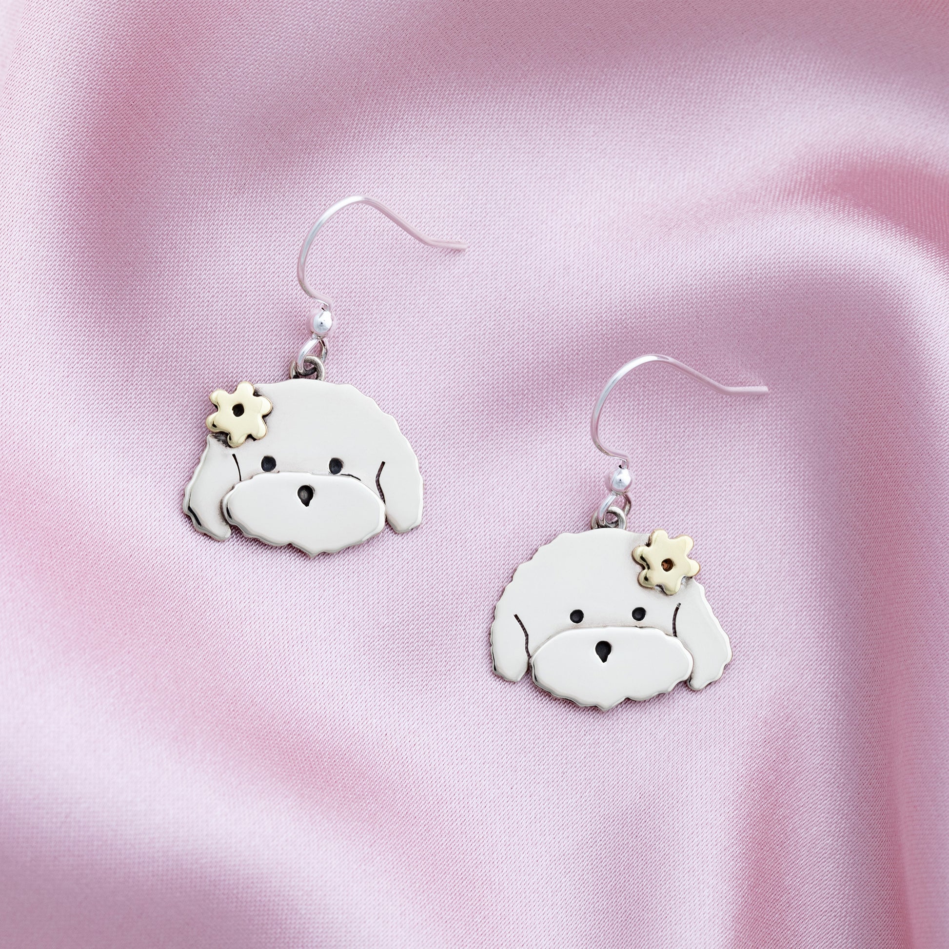 Pair of dog-shaped earrings on a pink fabric background