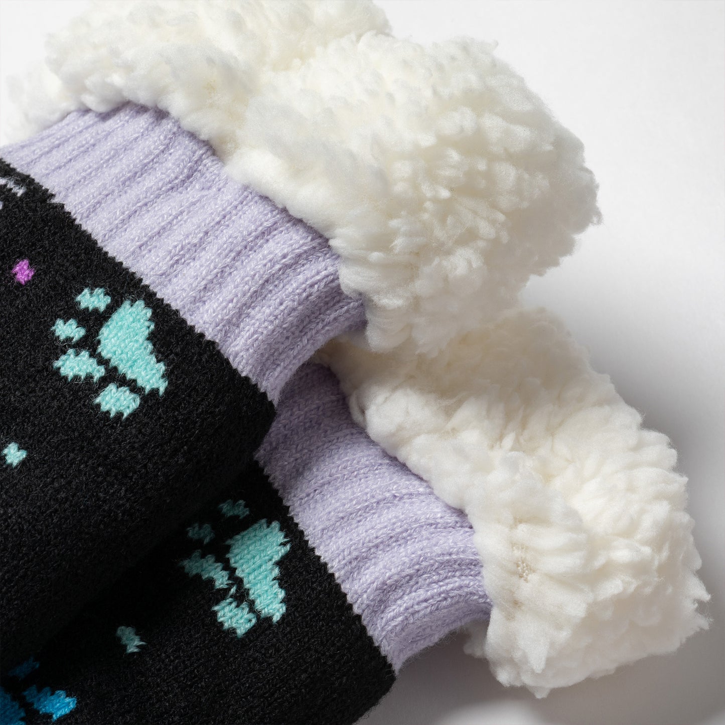 detail shot Pair of black with purple and blue polka dot paws Sherpa Fleece Lined Paw Print Cabin Slipper Socks with sherpa trim on a light gray background polka dot paws 