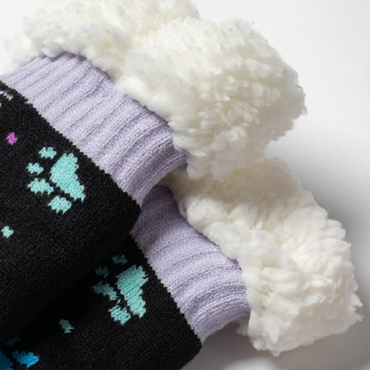 detail shot Pair of black with purple and blue polka dot paws Sherpa Fleece Lined Paw Print Cabin Slipper Socks with sherpa trim on a light gray background polka dot paws 