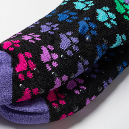 close up of Pair of rainbow paws Sherpa Fleece Lined Paw Print Cabin Slipper Socks with sherpa trim on a light gray background rainbow paws, detail shot of traction dots