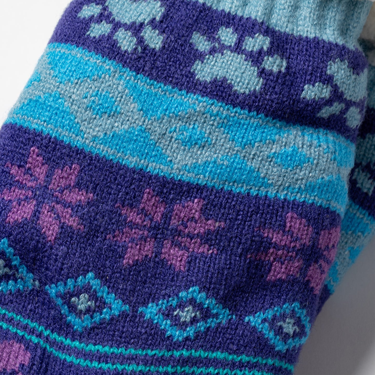 close up of knitted fabric blue and purple Sherpa Fleece Lined Paw Print Cabin Slipper Socks with sherpa trim  on a light gray background arctic paws pattern