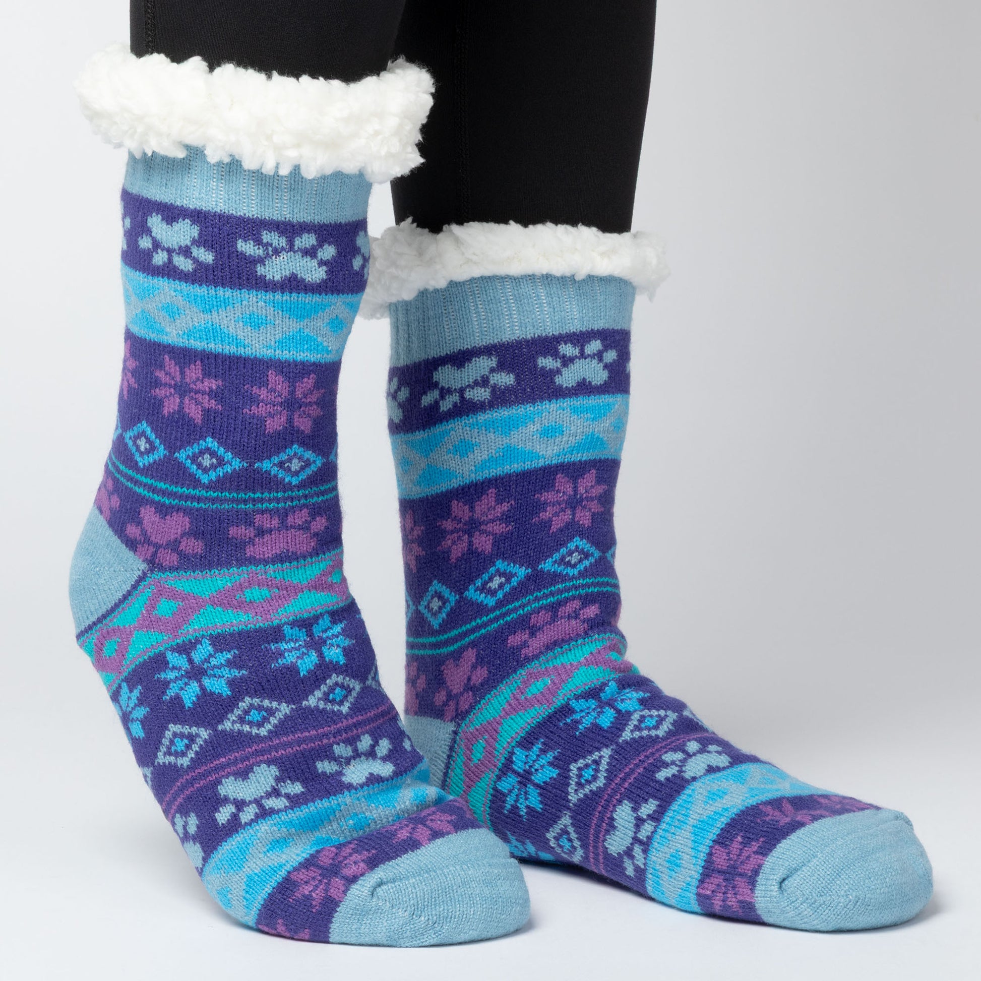 model wearing Pair of blue and purple Sherpa Fleece Lined Paw Print Cabin Slipper Socks with sherpa trim  on a light gray background arctic paws pattern