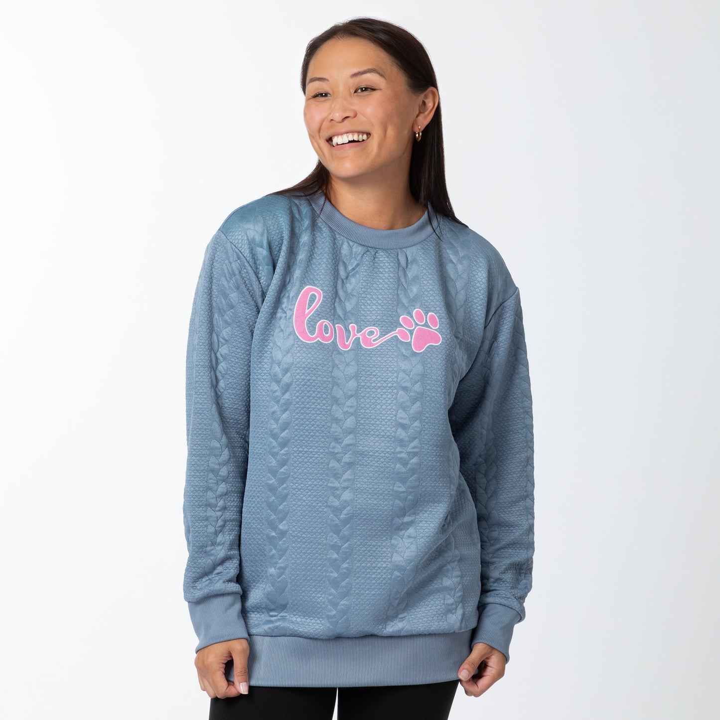 Woman wearing a blue sweater with pink 'love' and paw print design on a white background