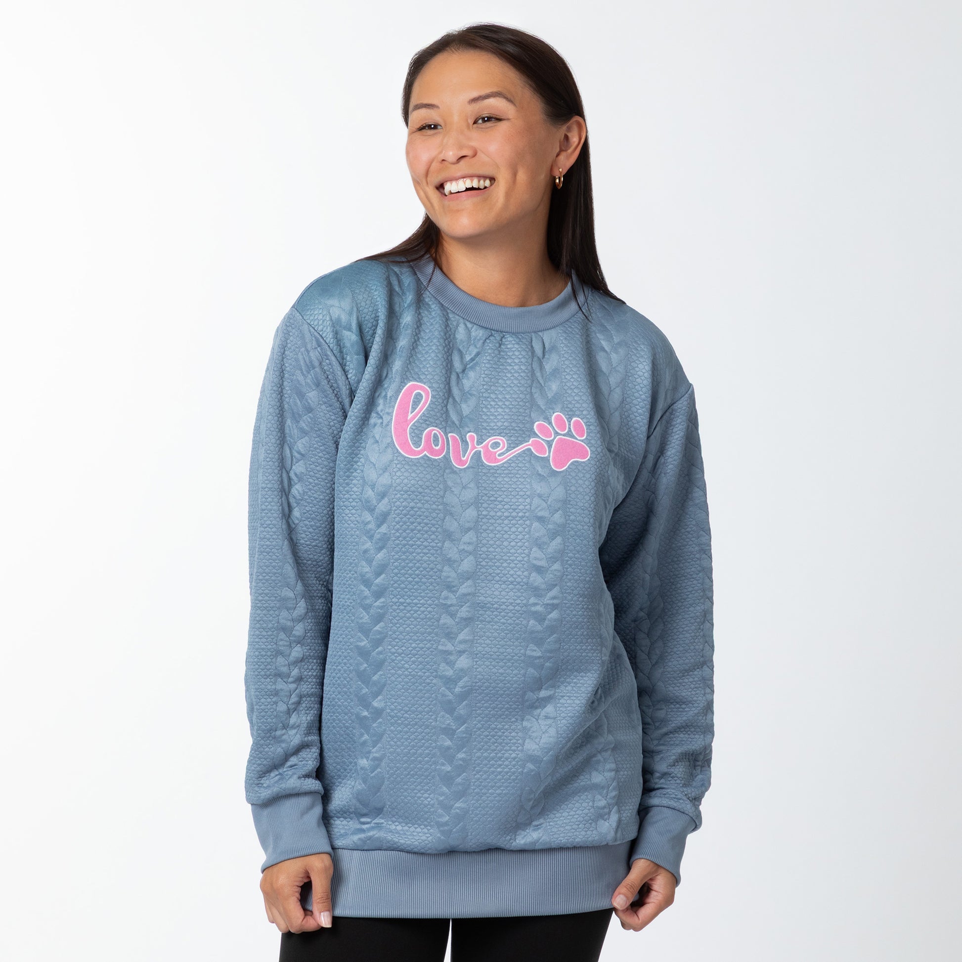 Woman wearing a blue sweater with pink 'love' and paw print design on a white background