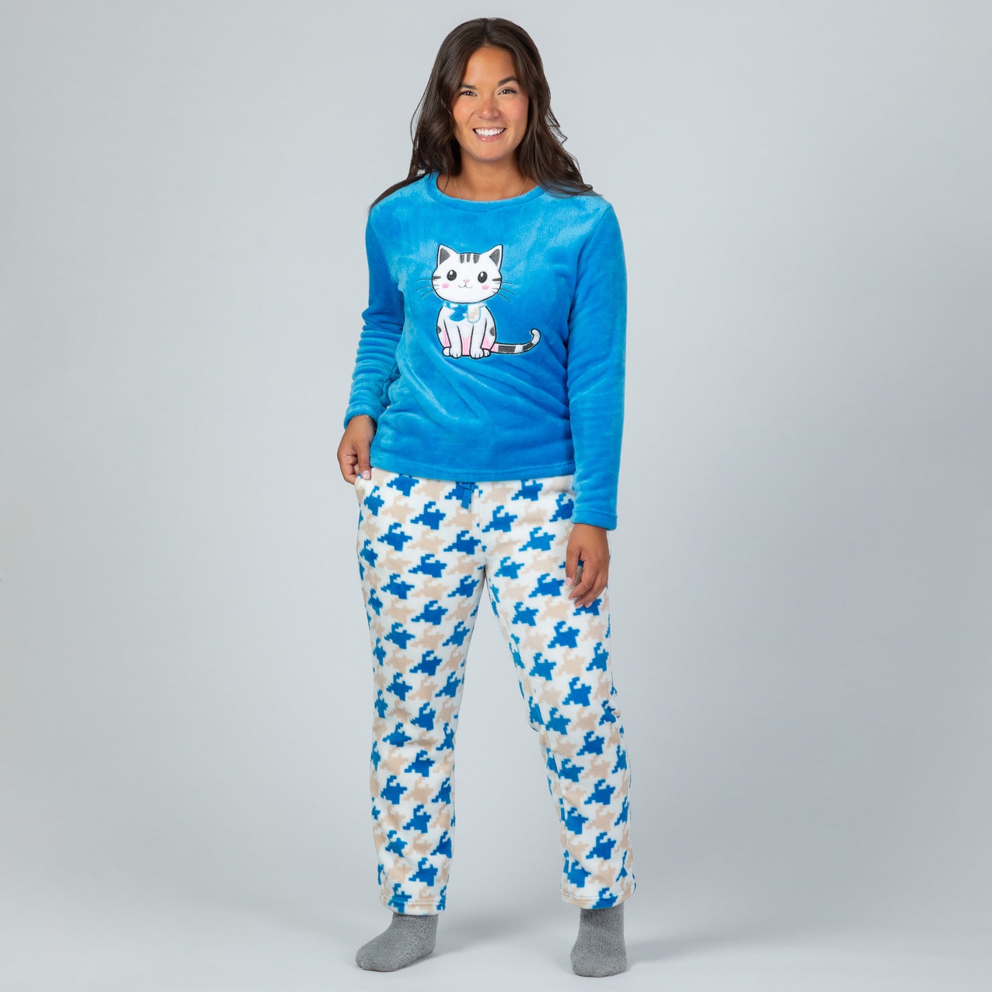 A woman wearing a blue long-sleeve top with an embroidered cute cat design and gray, blue and light blue houndstooth pattern. Design a blue cat in super cozy fabric, standing against white background