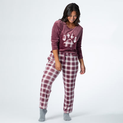 Woman wearing a velour pajama set— the top is a maroon long-sleeve shirt with a large plaid paw print. The pants are the same white and maroon plaid pattern as the paw print on the shirt. The shirt sleeves are rolled up to the elbows and the hem is tucked into the adjustable waistband of the pants.