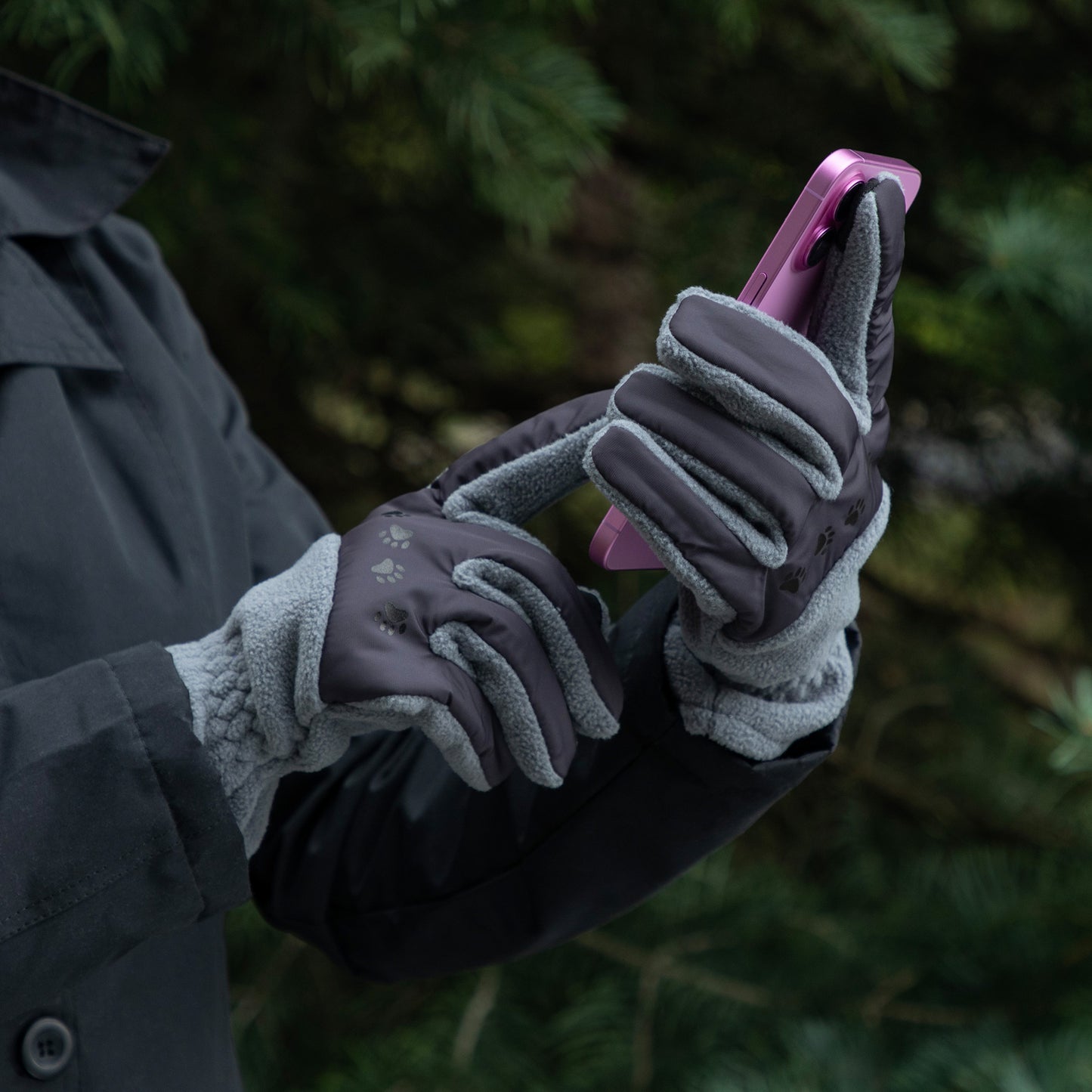 Person wearing gardening gloves holding a pink phone with a blurred green background