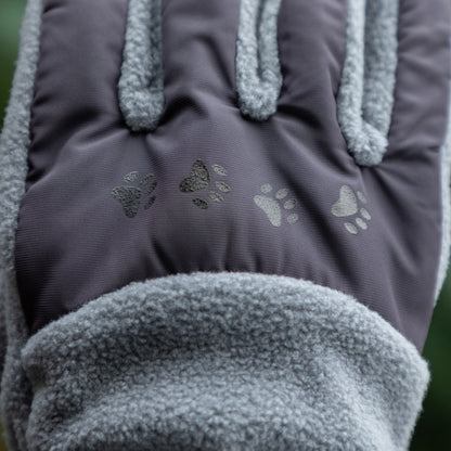 Close-up of a pair of gray gloves with paw print designs on a blurred green background