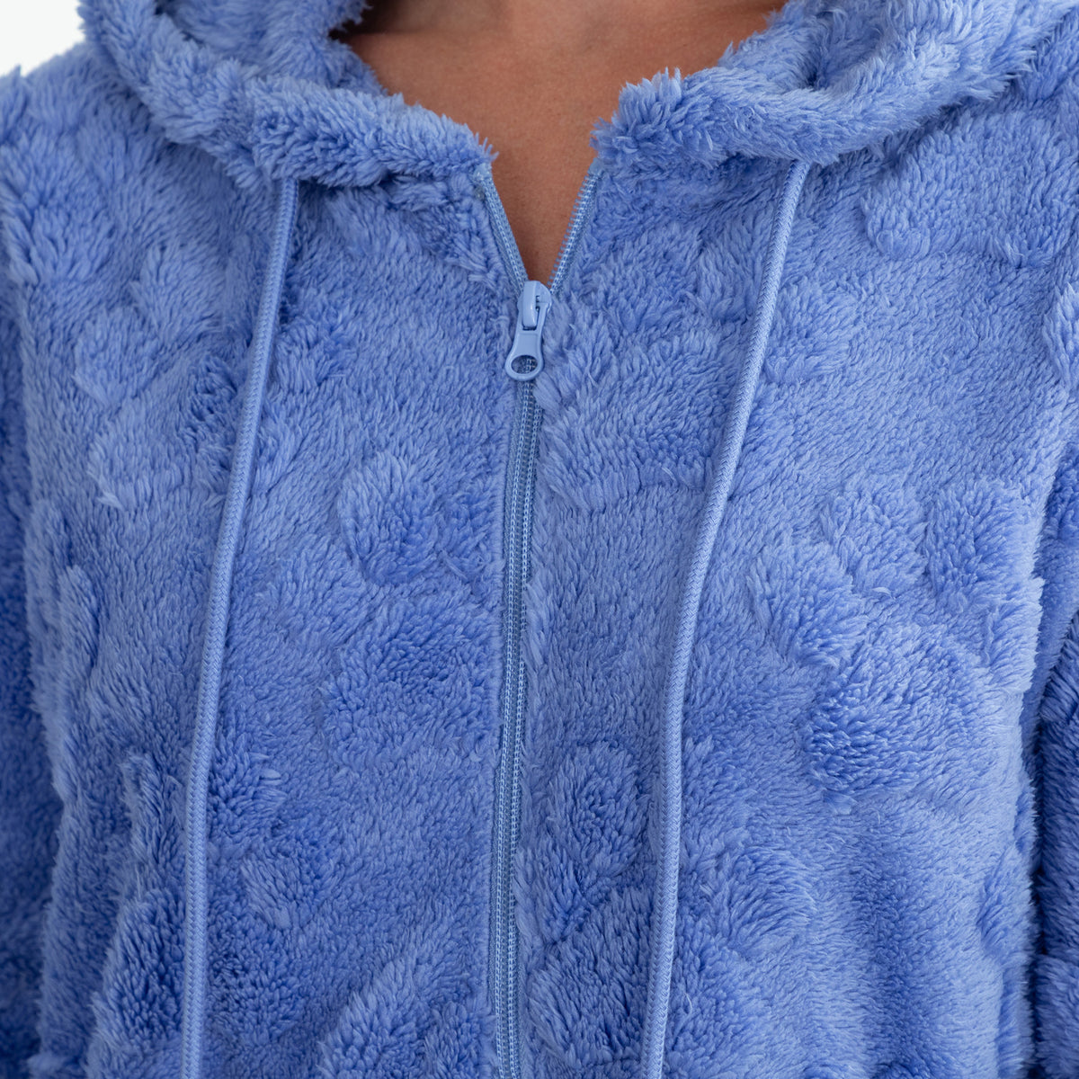 Close-up of a person wearing a plush zip-up hoodie in a dusty light blue color, showing the textured fabric, drawstrings, and zipper.