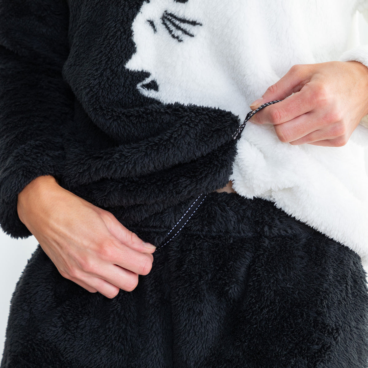 Close-up of a person wearing a plush black and white cat-themed robe, pulling the drawstring of the waist area.