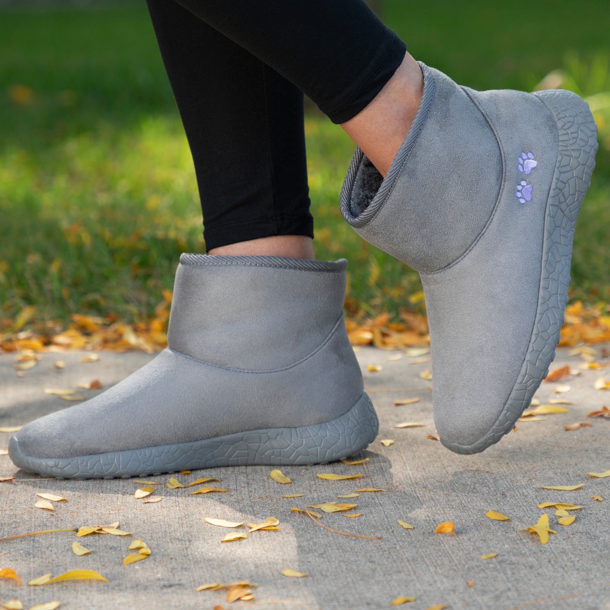 Gray slip-on boots worn outdoors on a grassy area with fallen leaves.