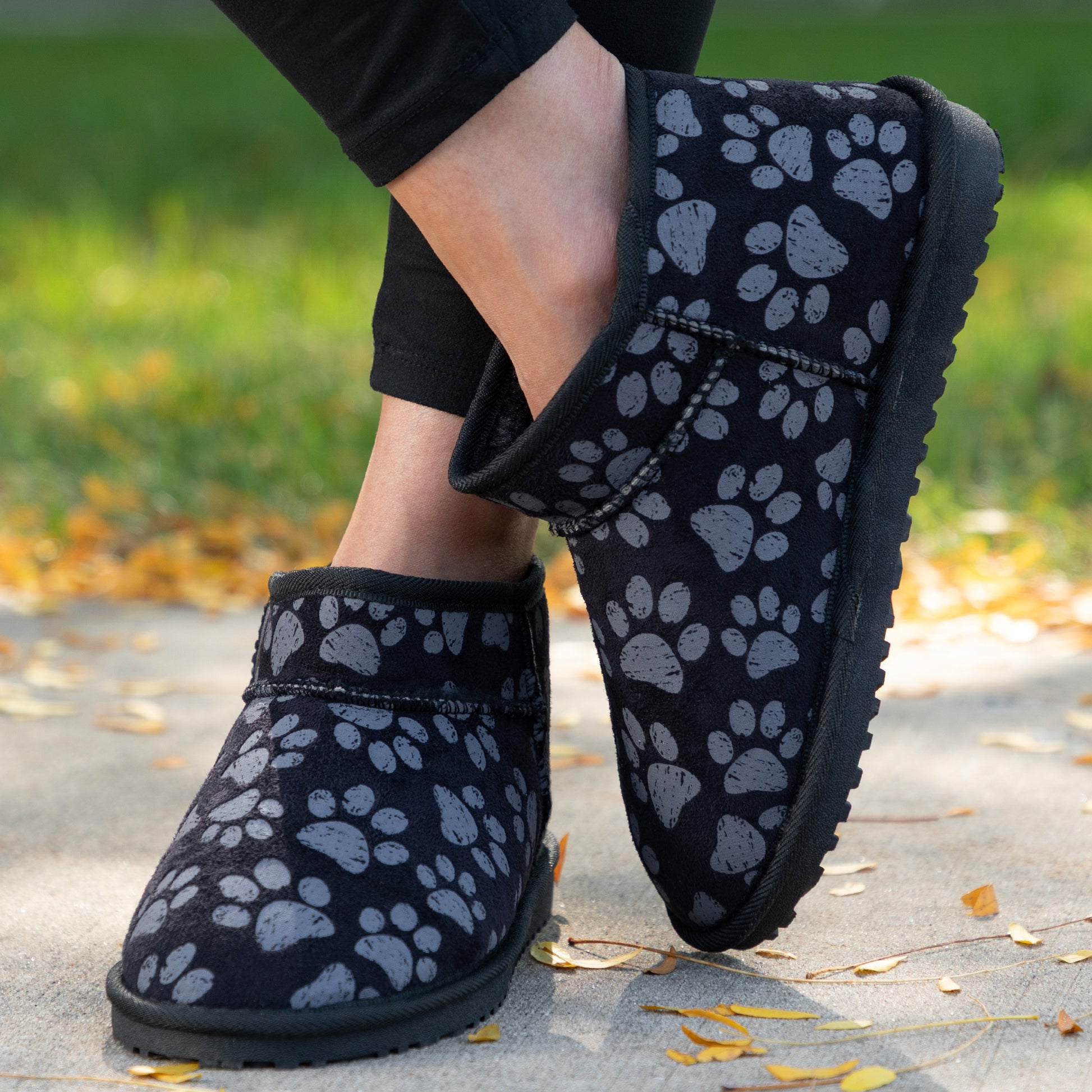 Black ankle boots with paw prints worn on a concrete surface with grass and leaves in the background