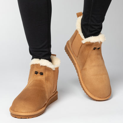 Tan suede boots with white fur lining worn by a person on a light gray background