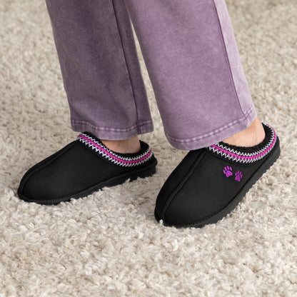 Black slippers with colorful trim and two embroidered paw prints on a carpeted floor.