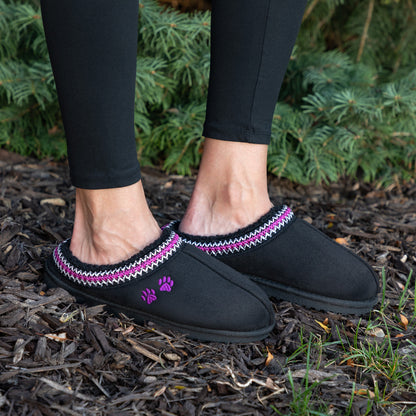 Black slipper shoes with purple accents worn outdoors on a mulched surface.
