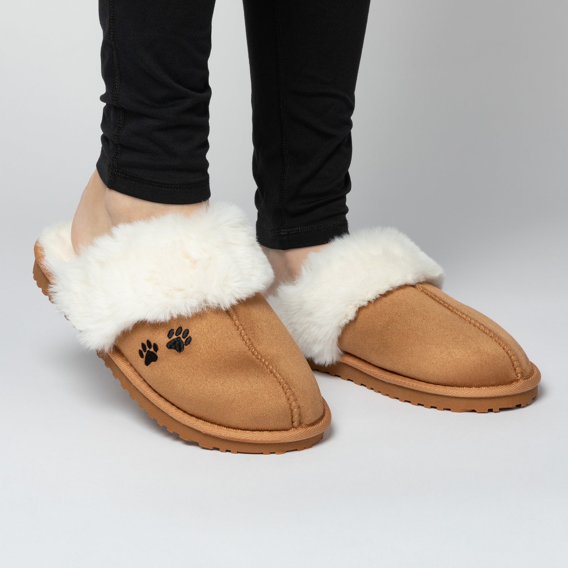 Tan slippers with white fur lining worn by a person on a light gray background