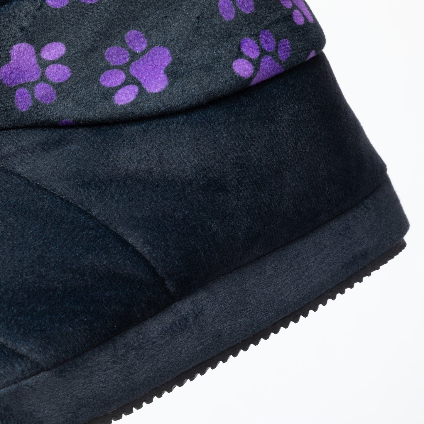 Close-up of a black slipper bootie showing the side profile, textured fabric upper, and a pattern of purple paw prints on the top edge against a white background.