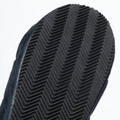 Close-up of a black textured rubber sole with a herringbone tread pattern, set against a plain white background.