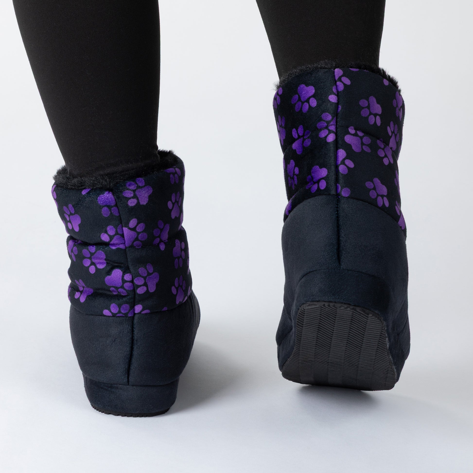 Black ankle boot slippers with purple paw print patterns on the cuffs, shown from the back on a light gray studio background.