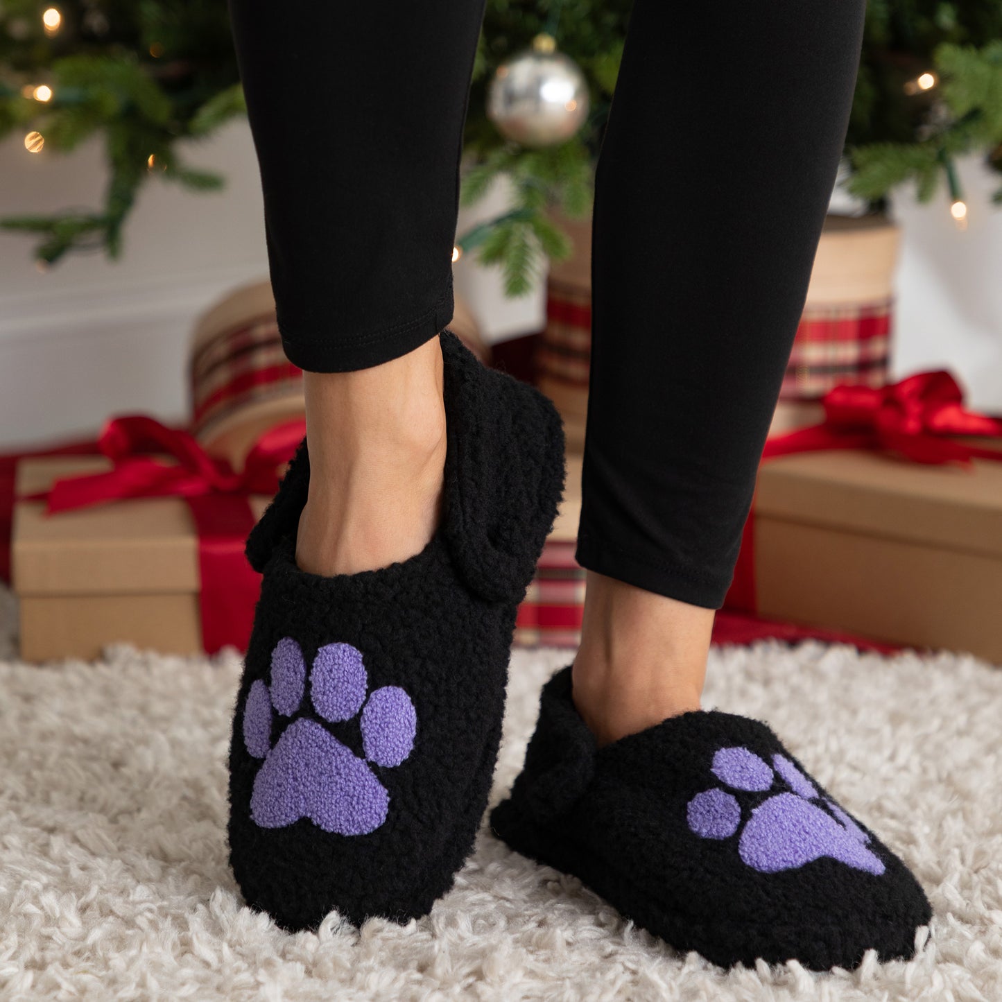 Black slippers with purple paw prints worn indoors with Christmas decorations in the background