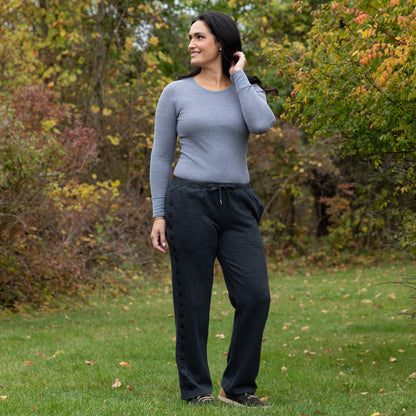 Woman standing outdoors in a park wearing a gray sweater and dark sweatpants.