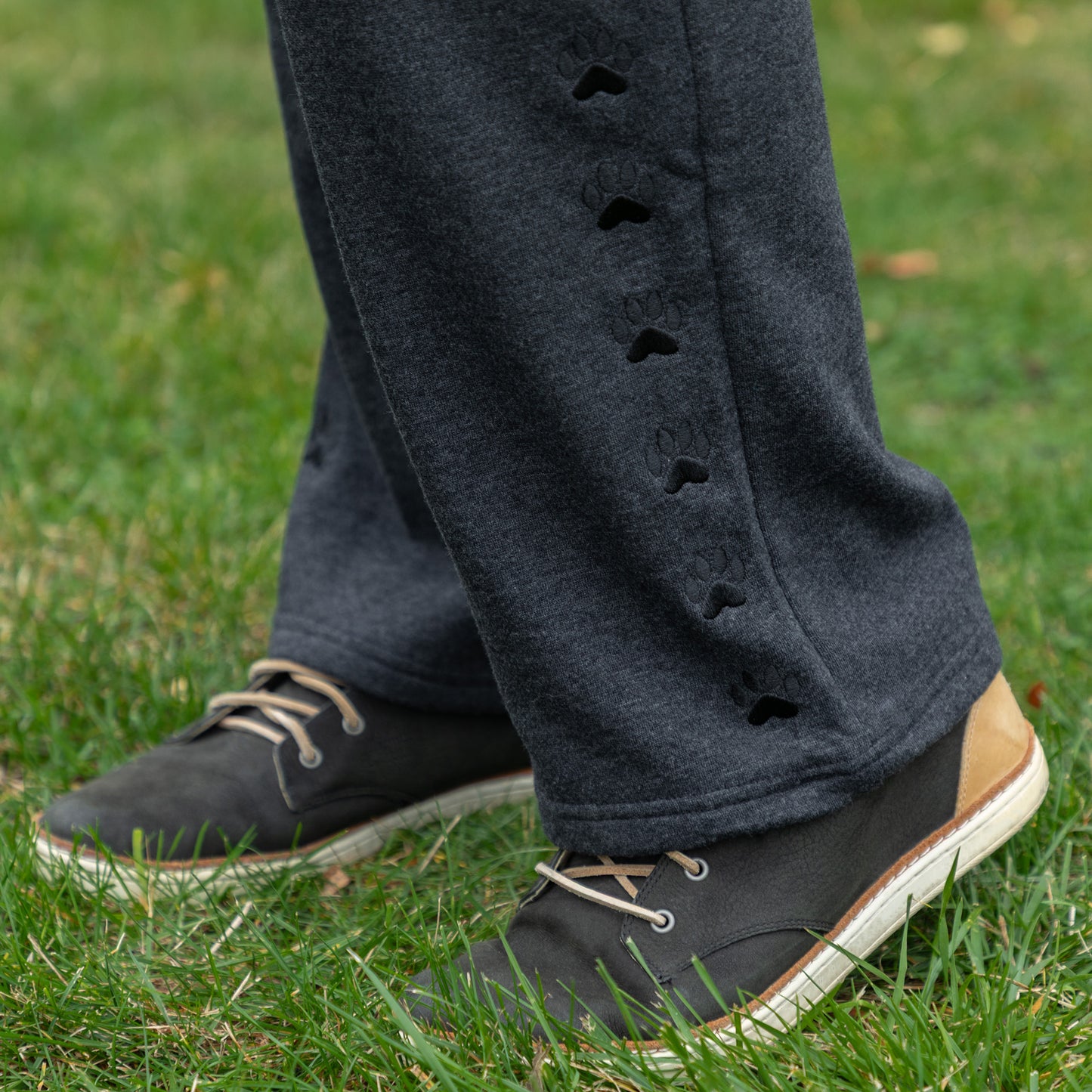 Person wearing dark gray pants with embroidered paw details and black shoes on grass