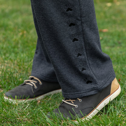 Person wearing dark gray pants with embroidered paw details and black shoes on grass