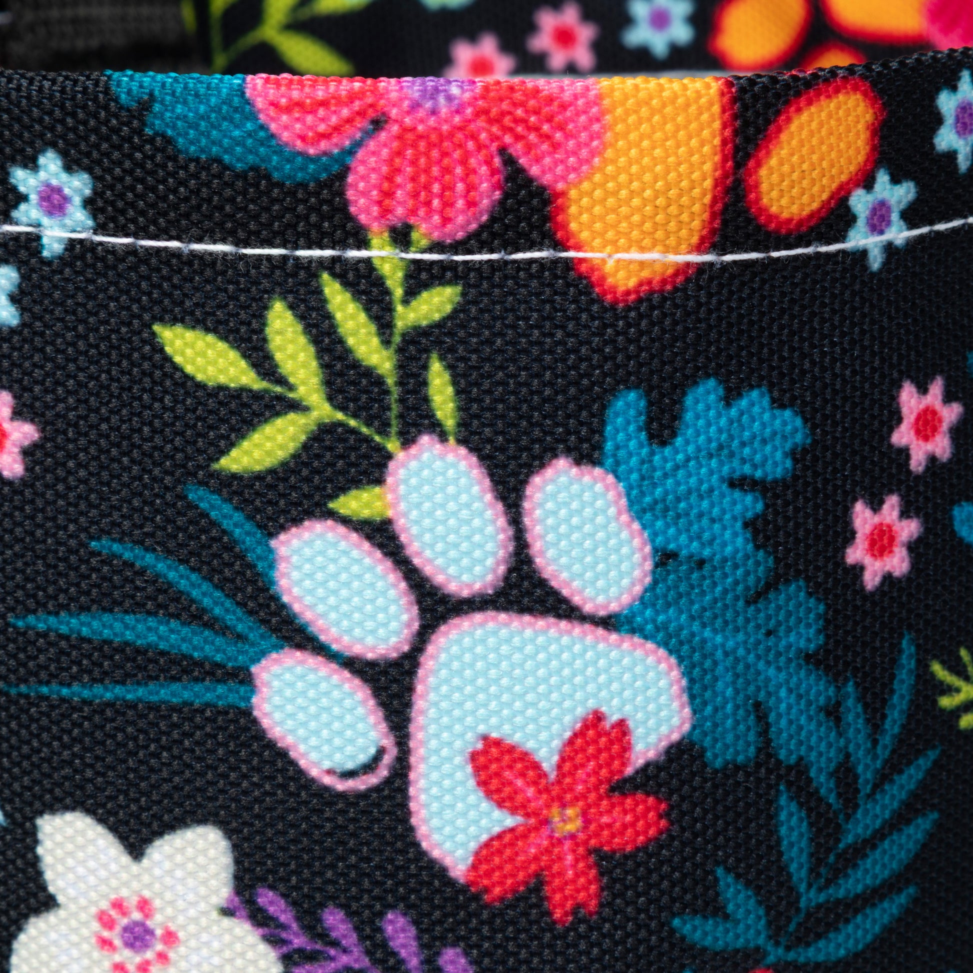 Close-up of a fabric with colorful floral and paw print designs on a black background.
