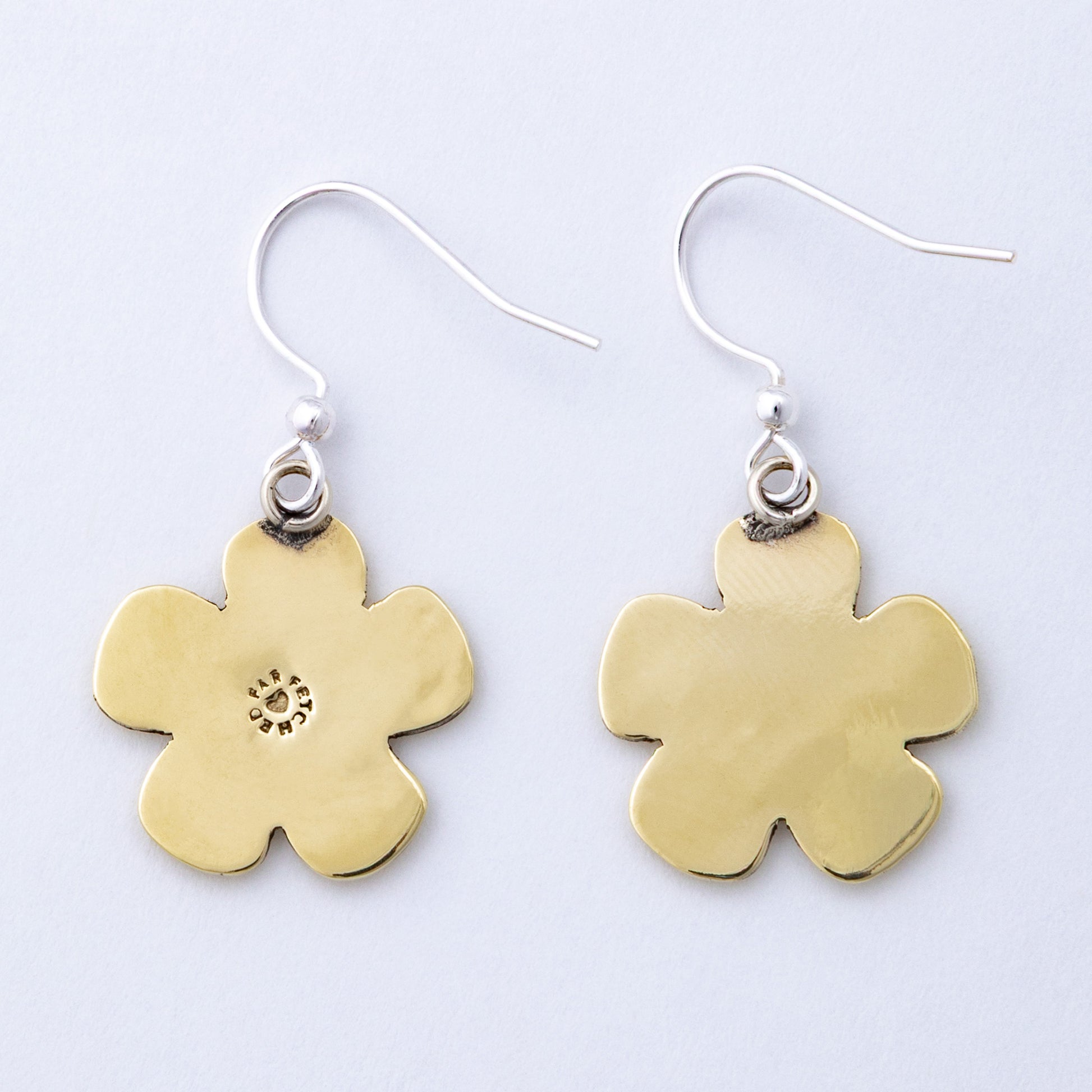 Brass back of flower-shaped earrings on a light gray background