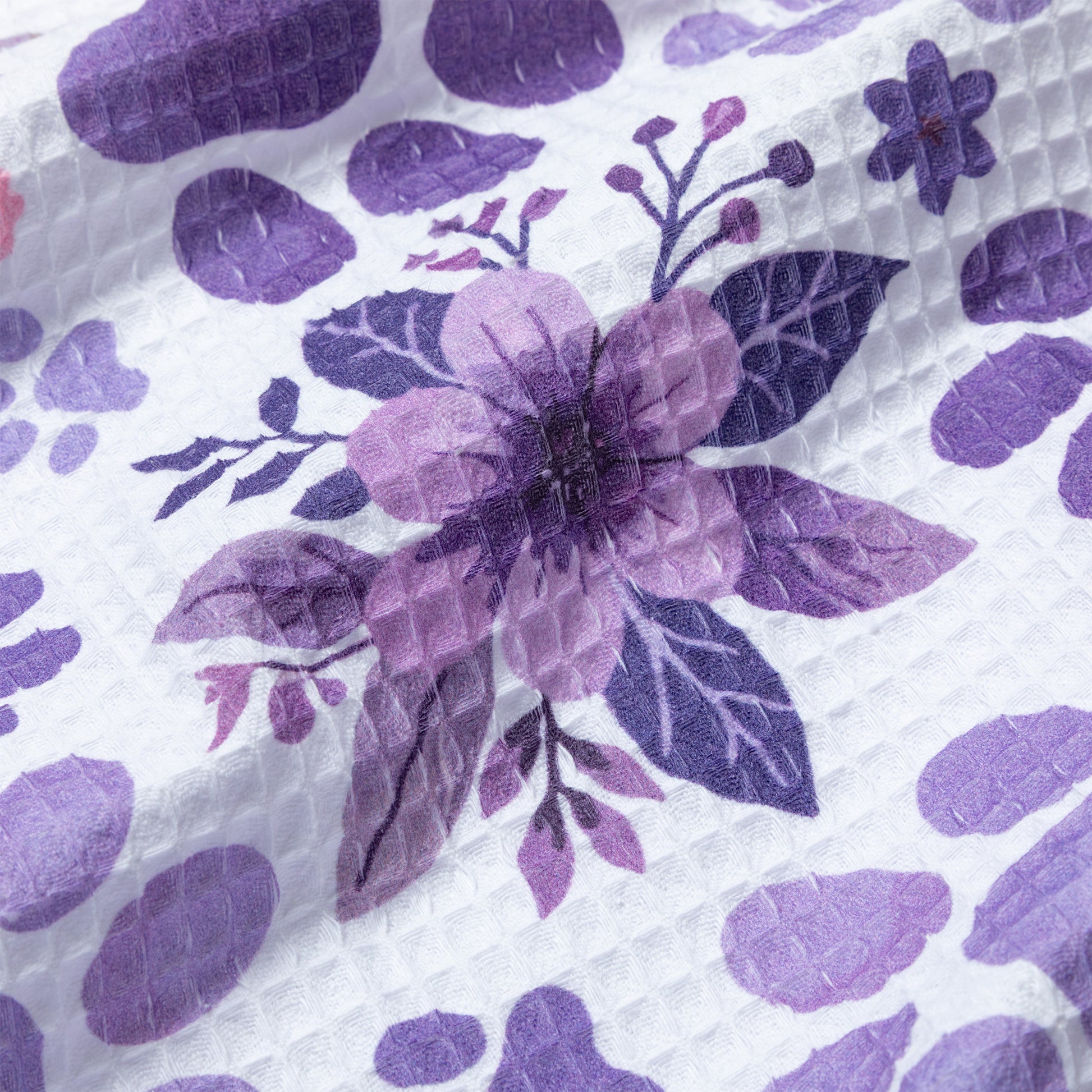 Close-up of a dish towel with purple floral design on a textured white background