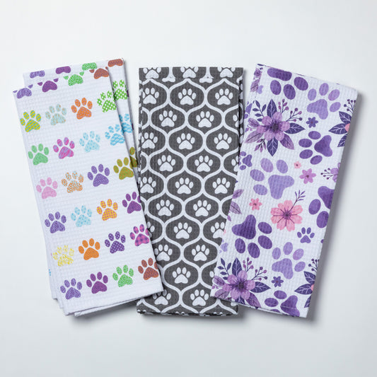 Three patterned towels with paw prints and floral designs on a white background