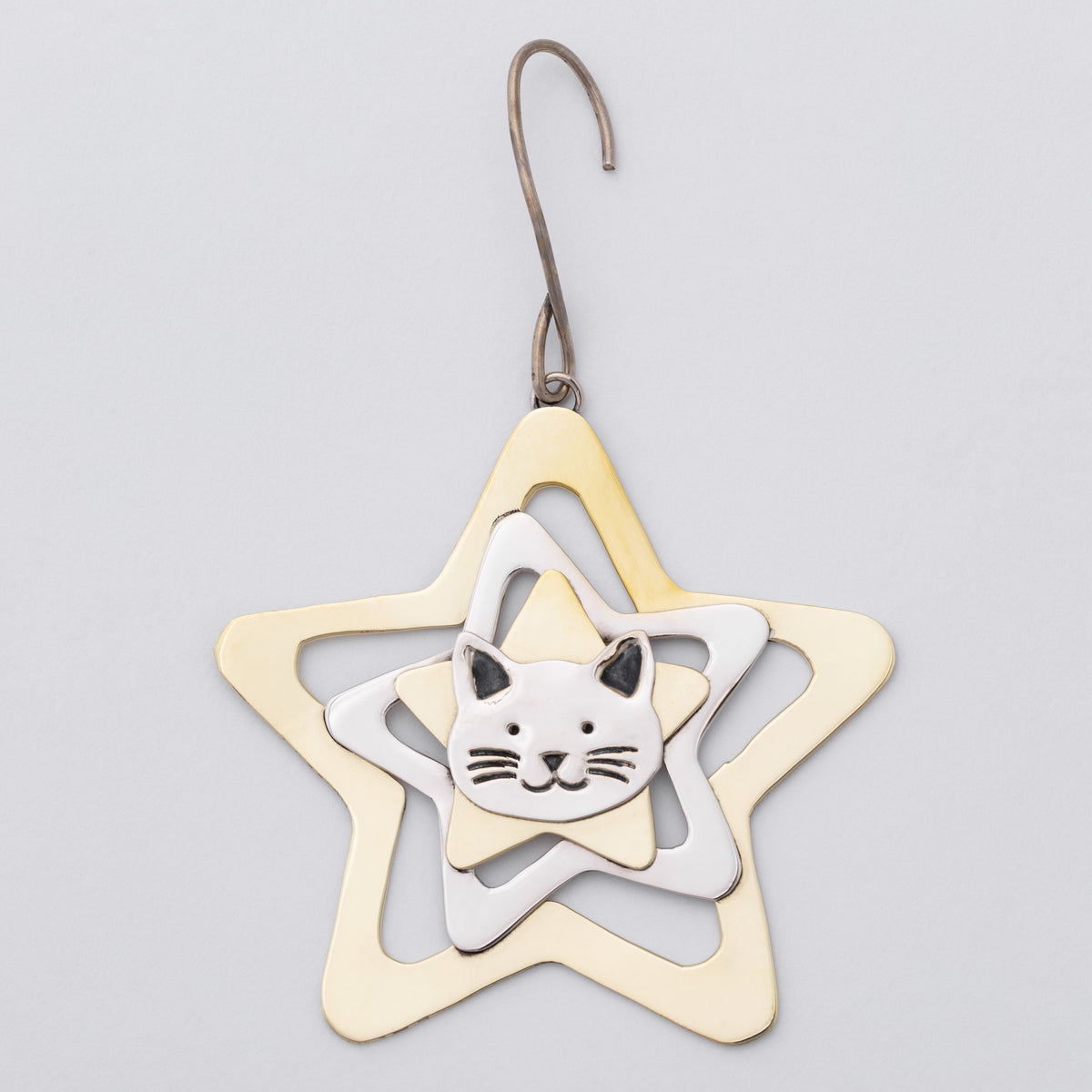A metal ornament shaped like a five-pointed star with a small cat face in the center, suspended from a hook against a light gray background.