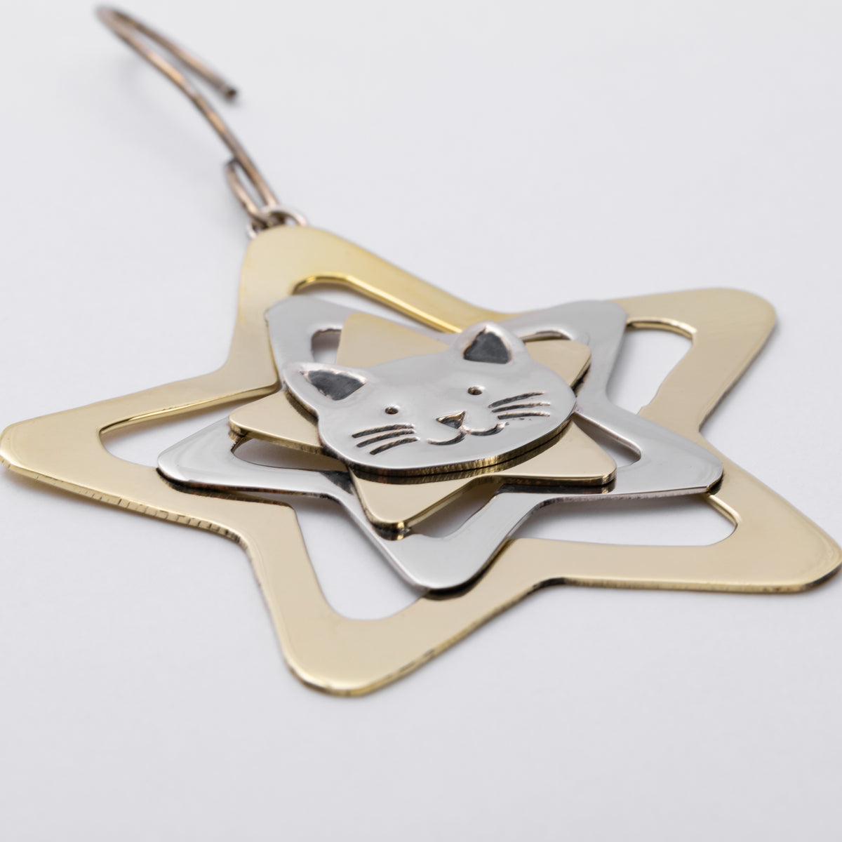 A metal hanging ornament featuring a gold star outline with layered silver elements, including a cat face and smaller star shapes, photographed on a plain light background.