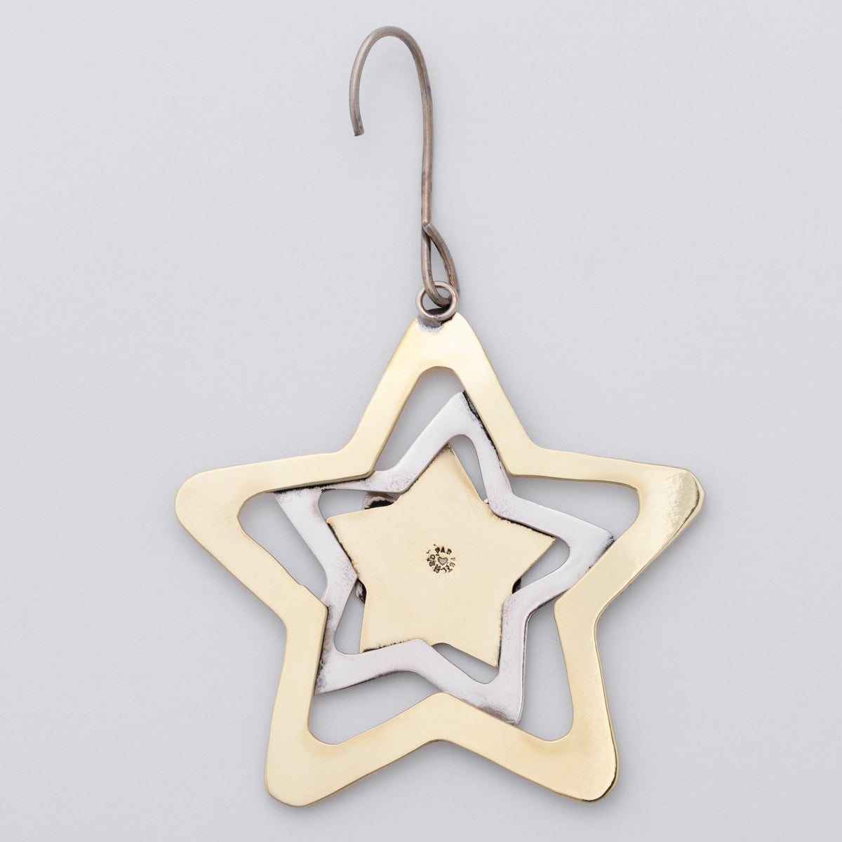 A star-shaped metal hanging ornament with concentric cutout layers in gold, silver, and white, suspended from a silver hook against a light gray background.