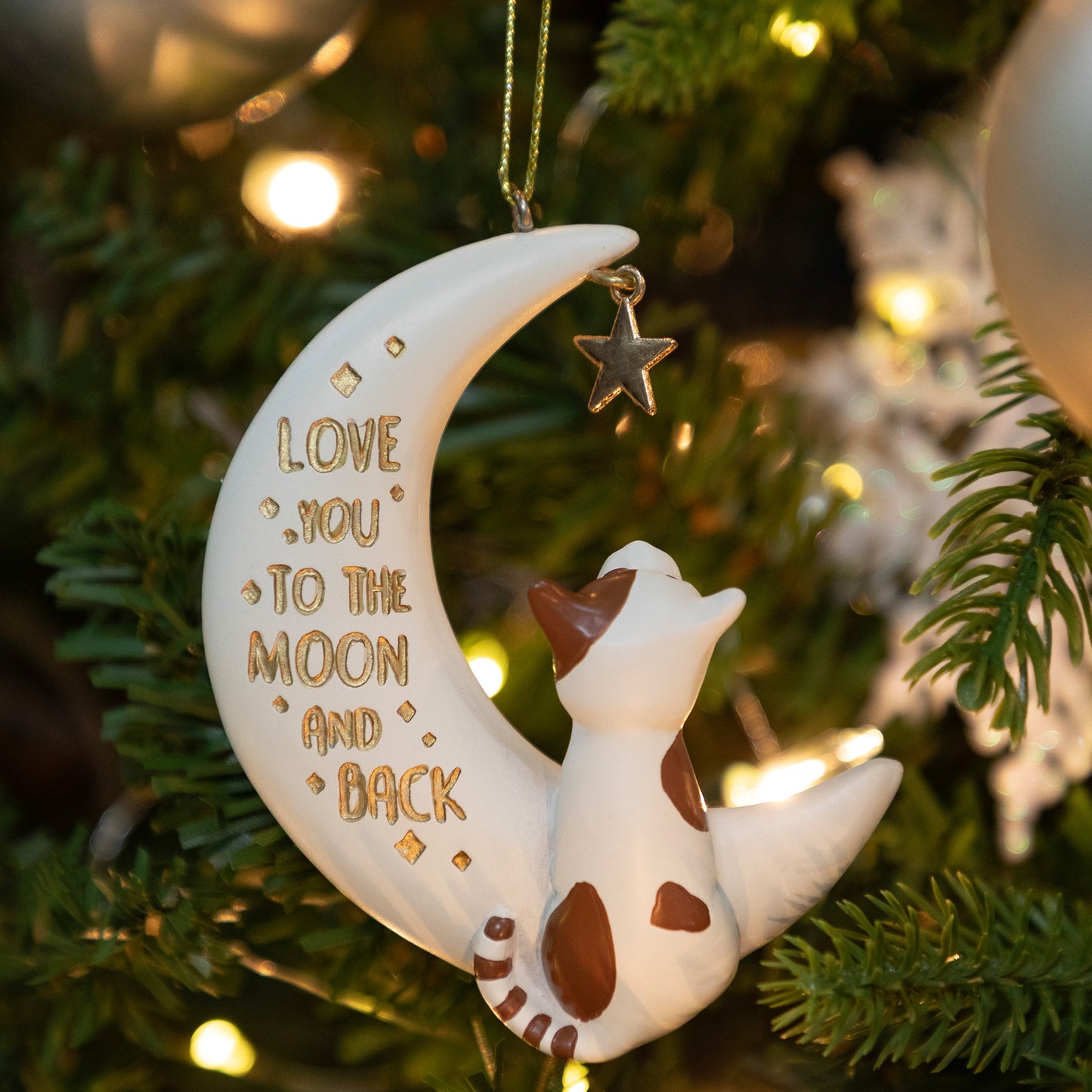 Decorative ornament with a cat on a moon, 'Love you to the moon and back' text, hanging on a Christmas tree.