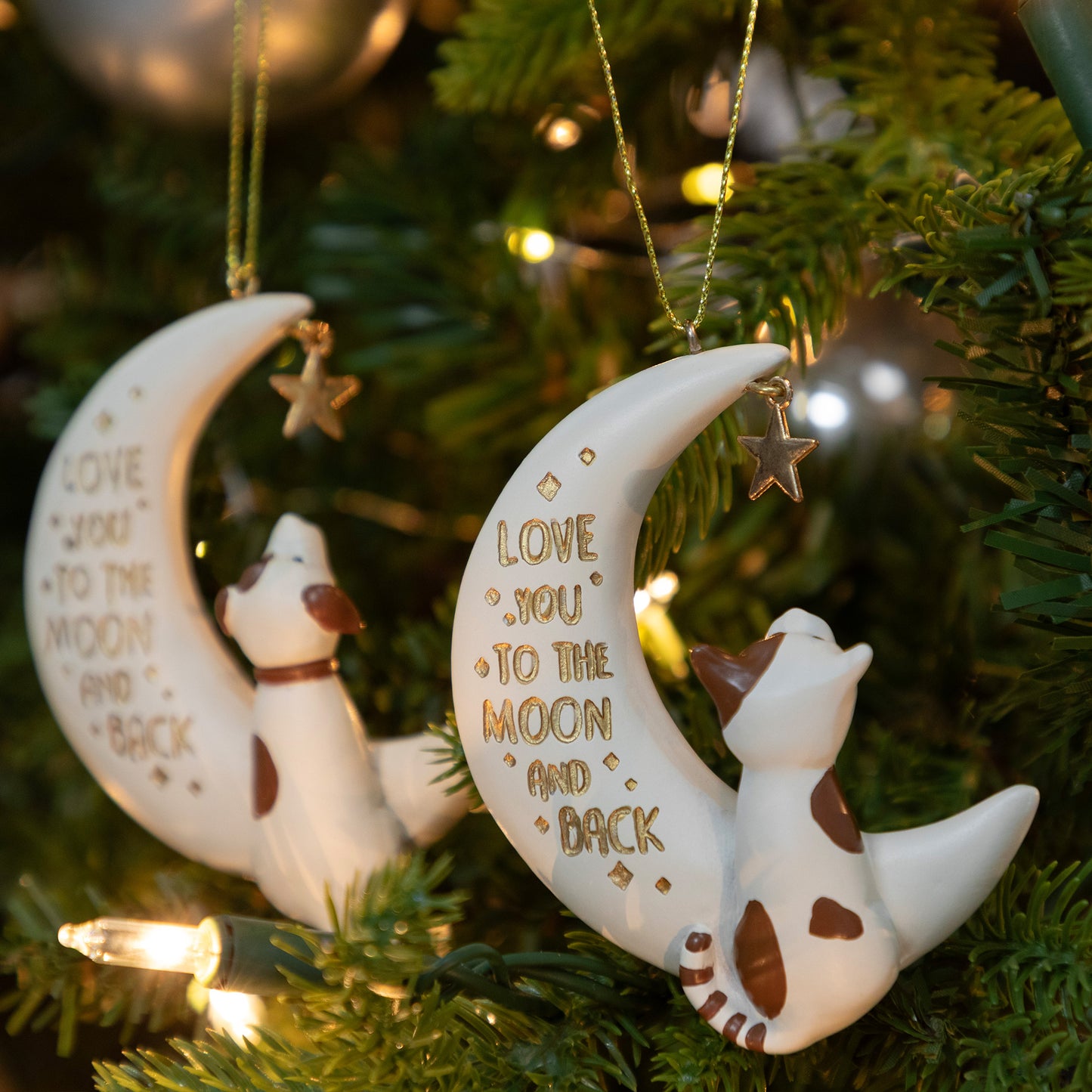 Decorative Christmas ornaments with a dog or cat on moons and 'Love you to the moon and back' text, hanging on a tree.
