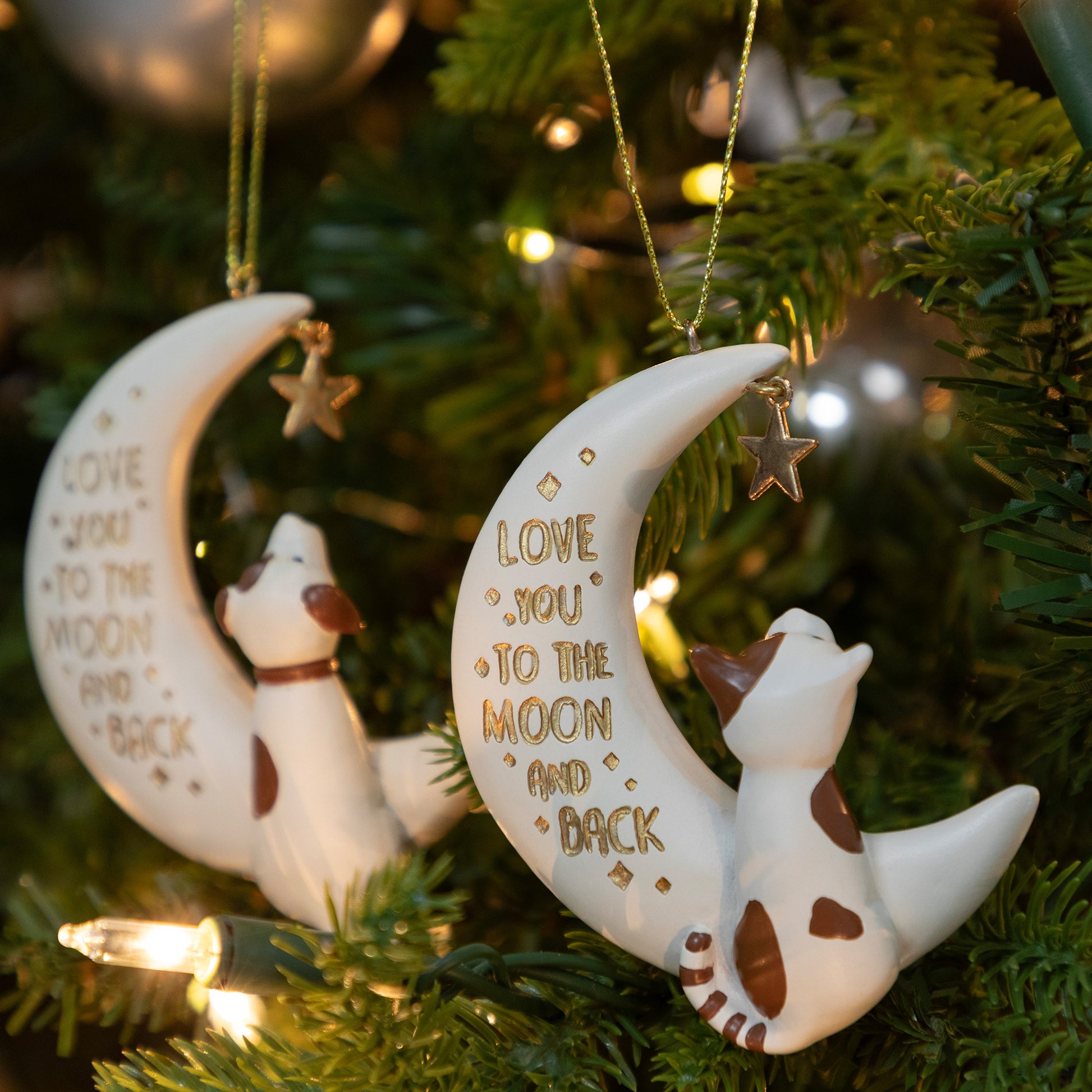 Decorative Christmas ornaments with a dog or cat on moons and 'Love you to the moon and back' text, hanging on a tree.