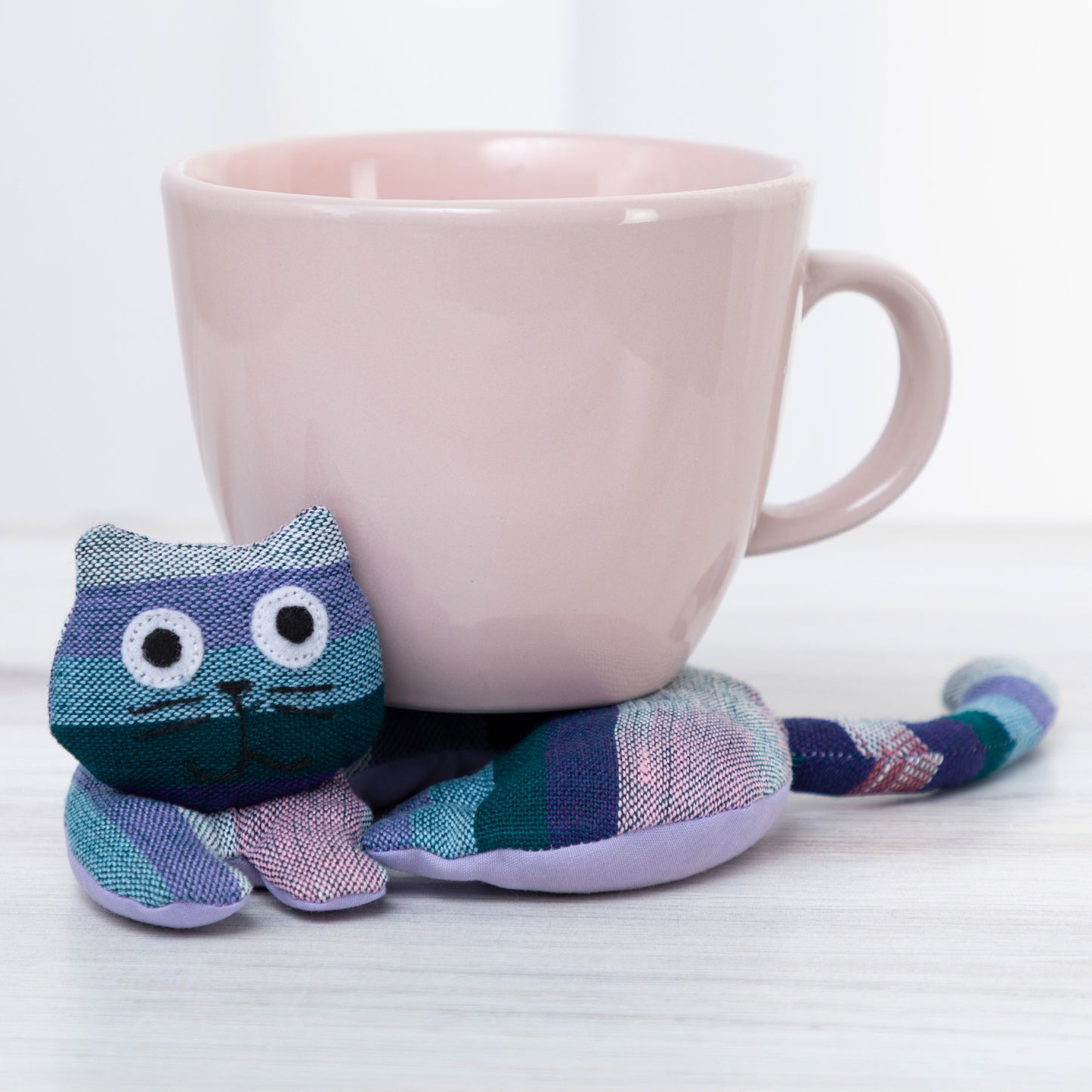 Cat-shaped knitted tea cozy on a pink mug with a white background
