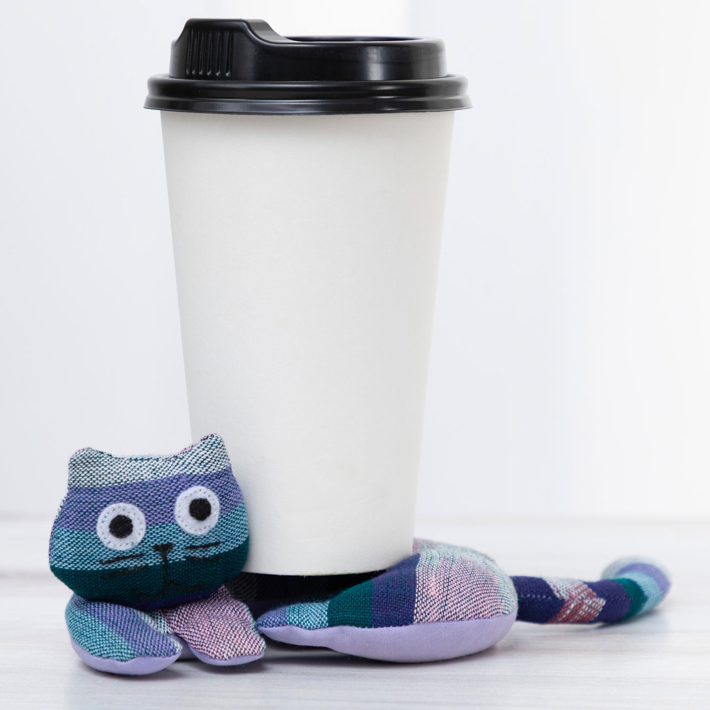 Plush cat shaped coaster with a coffee cup on a white background