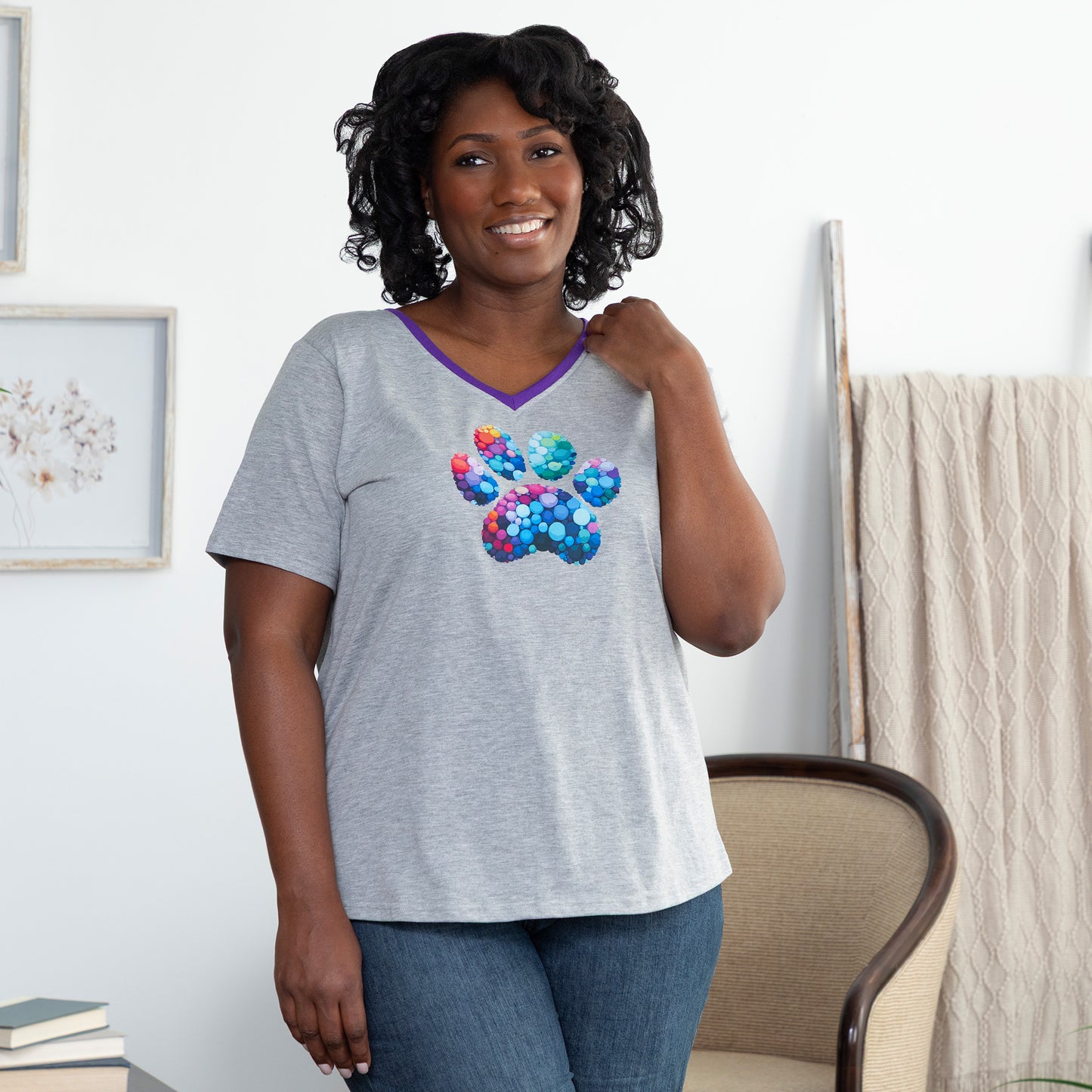 Woman wearing a gray v-neck t-shirt with a colorful paw print bubble design in a living room.
