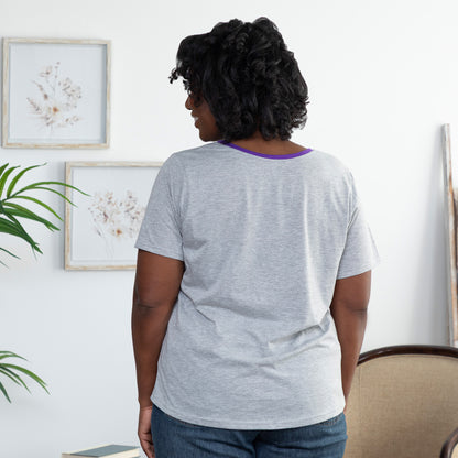 Woman wearing a gray t-shirt with a purple trim in a room with plants and framed pictures on the wall.