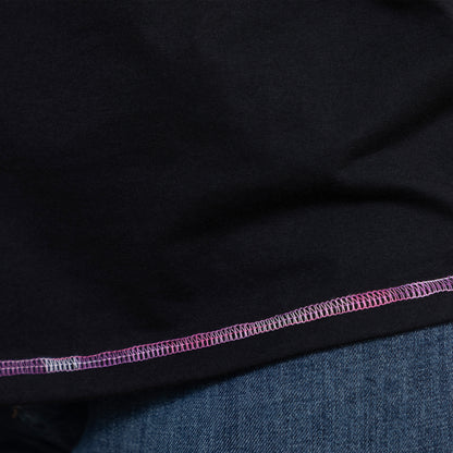 Close-up of black tee fabric with pink and purple contrast stitching detail at hem.