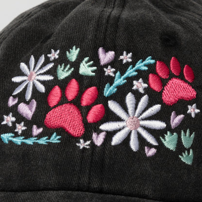Black cap with pink paw prints, flowers, and leaves on a white background.